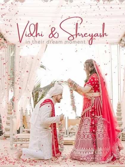 A dreamy Varmala moment where the groom gets on one knee to receive the garland from his bride, surrounded by a shower of petals.