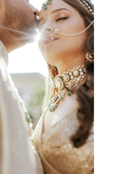A sun-kissed close-up on the wedding day. The details shine here, from the bride's intricate nath and jewelry to the groom's gentle kiss.
