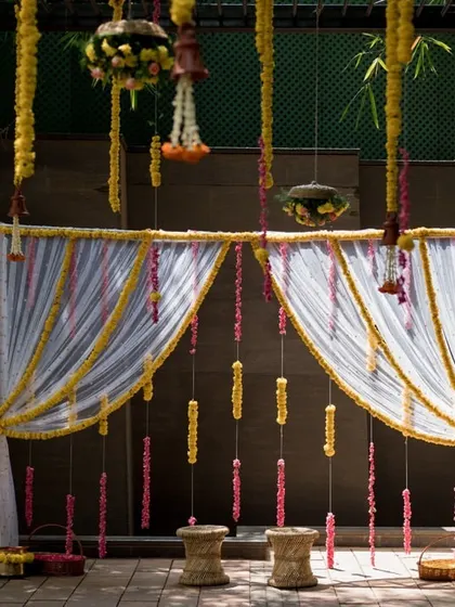 A simple yet elegant backdrop for an intimate ceremony, using sheer white curtains and strings of yellow and pink flowers.