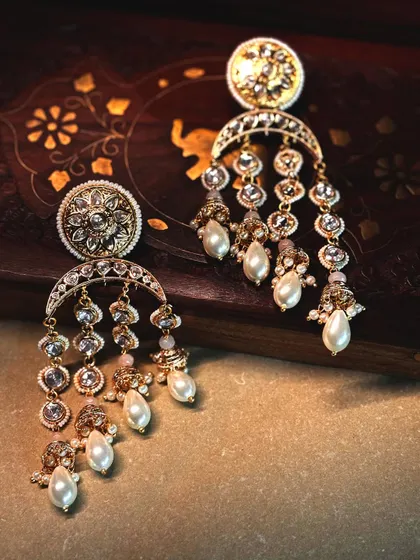 Elegant crescent-shaped earrings with dangling polki motifs and pearl drops, a classic design with a touch of movement.