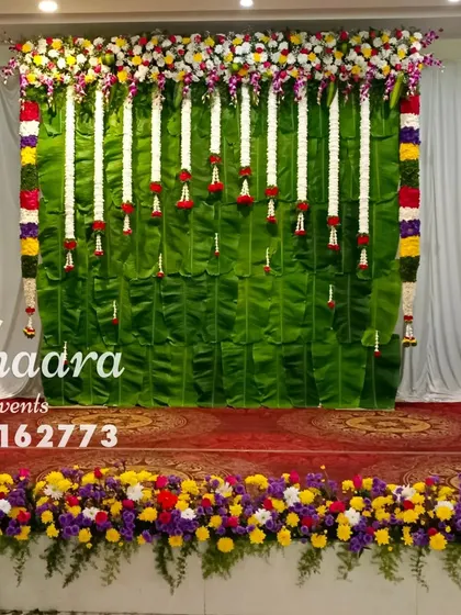 A traditional stage backdrop made entirely of fresh banana leaves. The look is completed with hanging garlands of white jasmine and colorful floral borders, perfect for baby showers and other ceremonies.