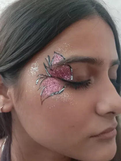A large, statement butterfly wing over the eye, filled with pink glitter and outlined in black and white.