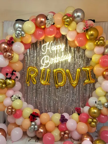 A beautiful pastel balloon ring with a silver shimmer curtain, personalized foil name balloons, and a central neon sign.