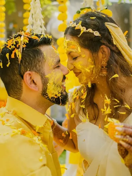 A romantic close-up of the couple, nose-to-nose, covered in haldi and flowers, capturing the intimacy of the moment.