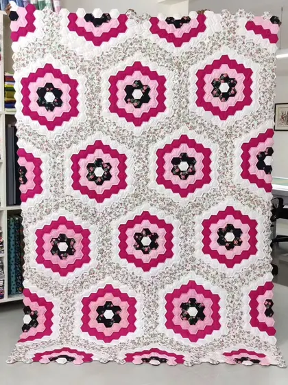 A beautiful "Grandmother's Flower Garden" quilt made of hexagonal pieces, in a striking pink and black colorway.