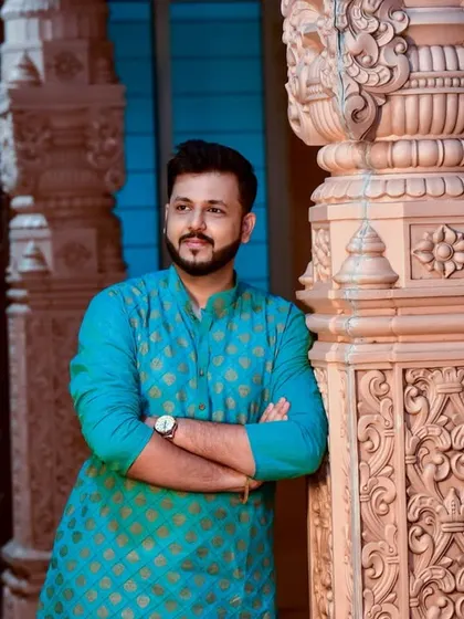 A stylish portrait of the groom in a patterned blue kurta, leaning against an intricately carved pillar.