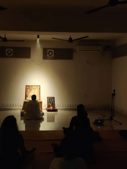 A wide view of the hall during a Sadhguru Sanidhi process. The room is filled with people sitting in stillness, their focus on the Guru's presence at the front.