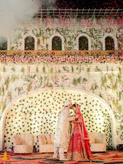 We believe in creating fairytale moments. This shot, with the couple sharing a kiss under a grand floral arch as petals rain down, showcases the cinematic and luxurious scale we bring to wedding photography.