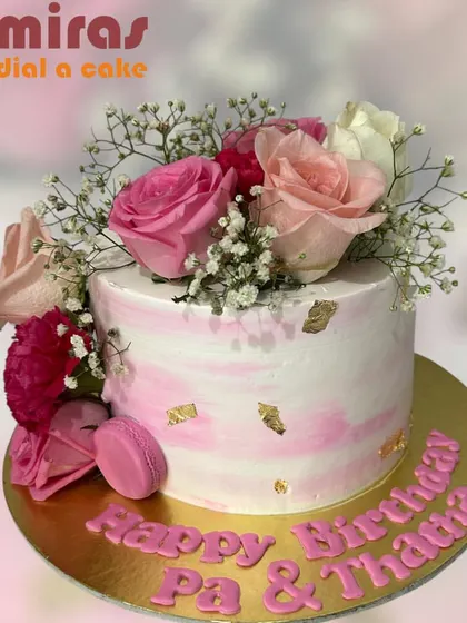 A beautiful cake with a pink marble buttercream finish, adorned with fresh roses, baby's breath, and delicate gold leaf. A single pink macaron adds a touch of modern elegance.