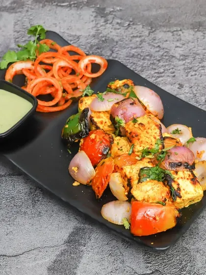A plate of our delicious Paneer Tikka, grilled with chunks of onion, tomato, and capsicum. It's a perfect, healthy starter for any meal.