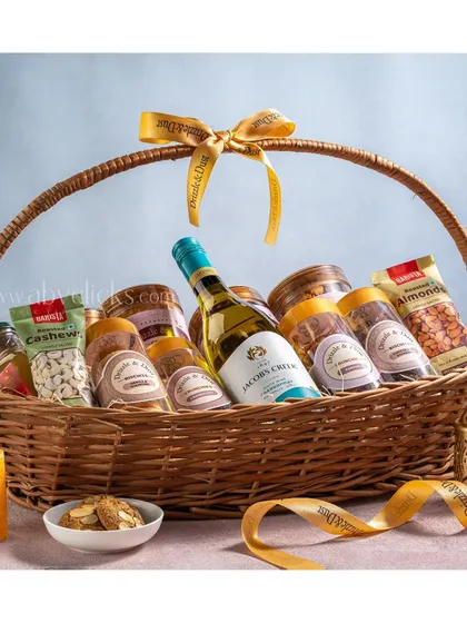 A beautifully arranged gift basket with wine and a variety of snacks, tied with a branded ribbon.
