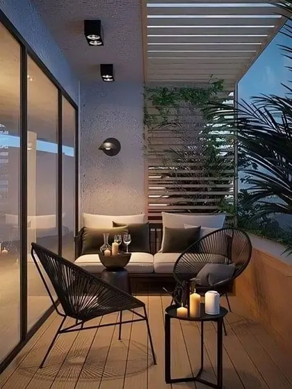 A chic and modern balcony with stylish black rope chairs and a sofa. The wooden deck and slatted privacy screen create a contemporary look, perfect for evening relaxation with candles.