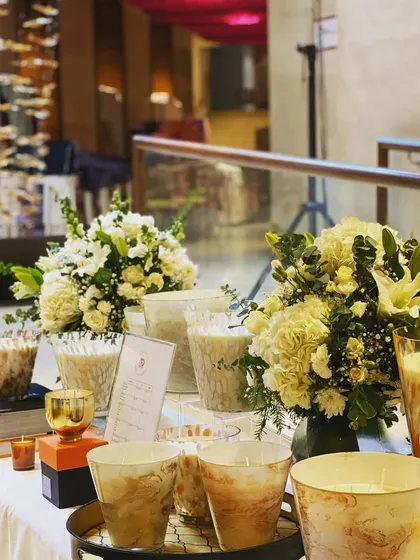 For this display table, I created two matching bouquets with white flowers and fresh greens to complement the products. Using multiple smaller arrangements can be just as effective as one large one for events or pop-up stalls.