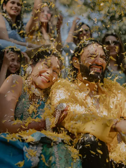 A joyful shot of the couple laughing together, covered in yellow petals.