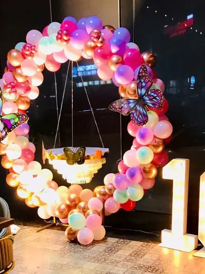 A unique 10th birthday setup with a chandelier cake stand inside a butterfly-themed balloon ring. The decor uses marquee numbers and a vibrant color palette.