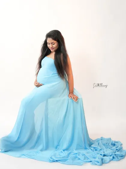 A serene portrait of a mother-to-be in a light blue gown. The simple white background and her gentle smile create a peaceful and classic maternity image.
