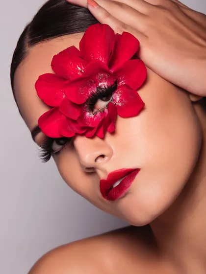 A classic glamour look with a bold red lip and dramatic lashes, made even more striking with a large red flower over one eye.