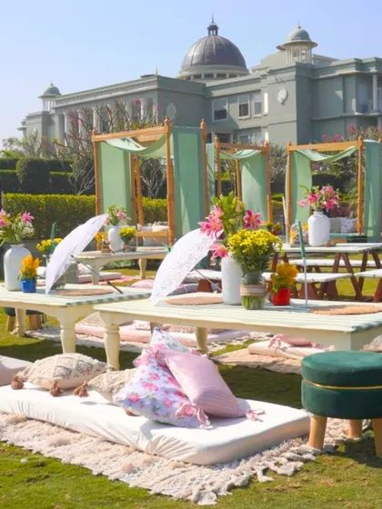 A low-seating lounge area with mattresses and cushions on the grass, paired with elegant canopy beds, offering a blend of comfort and style for a relaxed event.