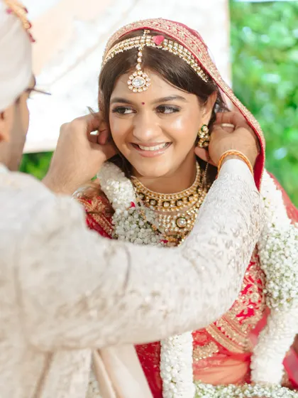 A sweet, intimate moment. This close-up highlights her dewy skin, soft smile, and the beautiful details of her bridal jewelry and makeup.
