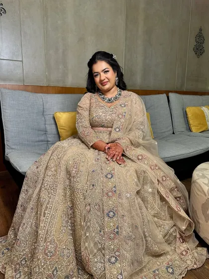 A regal reception look. The bride is seated, showcasing her magnificent lehenga. Her makeup is subtle yet glamorous, with a focus on flawless skin and defined eyes.