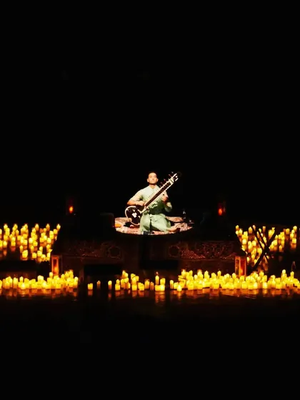 A wide shot of a candlelit performance, showing the scale and beauty of the 'Sitar for Mental Health' setup.