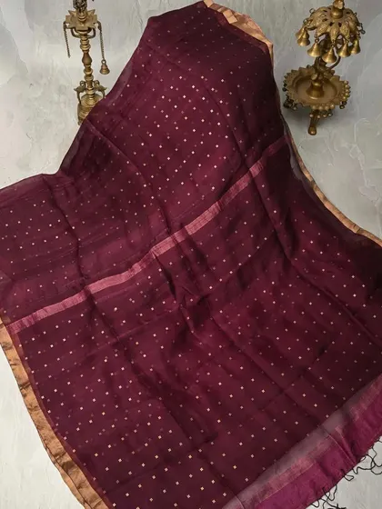A deep maroon Muslin silk saree with delicate gold butis. The fabric is exceptionally fine and breathable, offering a look of understated luxury.