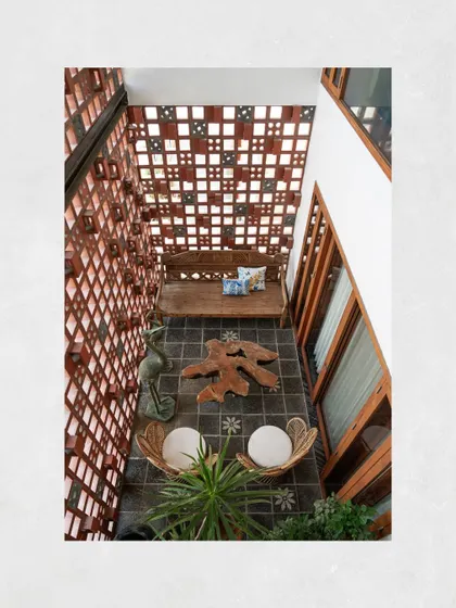 An overhead view of a balcony at Kamala Residence, showing the interplay of the terracotta breeze block wall, natural stone flooring, and reclaimed teak furniture.