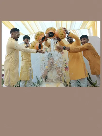 A fun and energetic moment as the men of the family pour water over the bride during the Haldi ceremony.
