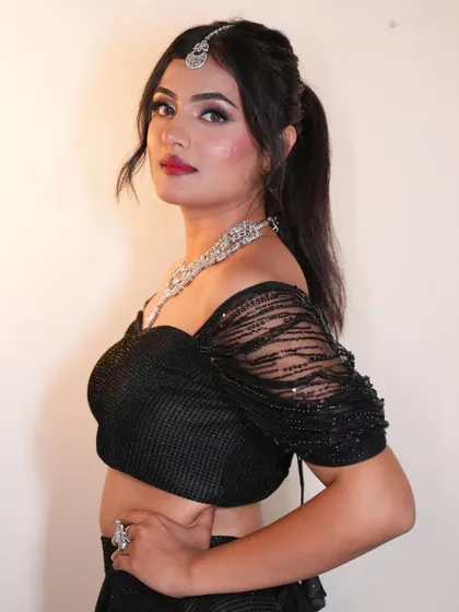 A side profile of the model wearing the black shimmer lehenga, highlighting the flattering cut of the off-shoulder blouse and the elegant silhouette.