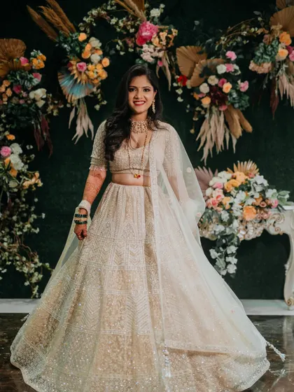 A full-length portrait of Sejal at her reception. Her beautiful ivory lehenga and radiant smile are set against a stunning floral backdrop.