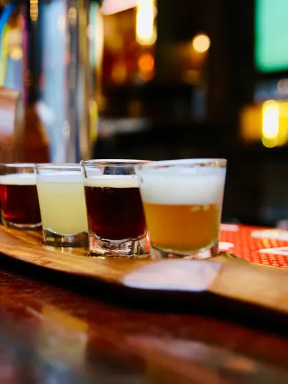 A beer flight, perfect for showing variety. This close-up shot highlights the different colors and textures of four distinct craft beers, inviting customers to try a tasting platter.