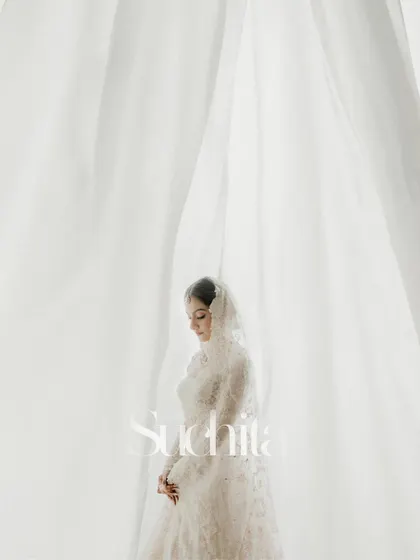 A beautiful, ethereal portrait of the bride, Suchita. The soft white curtains create a dreamy, light-filled backdrop that perfectly complements her delicate white lehenga.