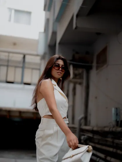 A profile shot of a model in a chic white outfit. The urban background is blurred, keeping the focus on her stylish look.