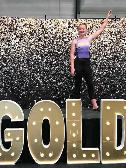 An Xcel Gold gymnast waves from the stage at the regional championships.