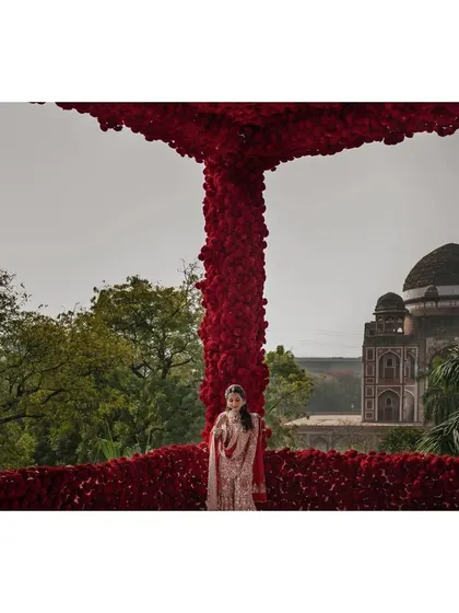 A stunning portrait of the bride, Nandini, framed by a massive arch of red roses, with Humayun's Tomb in the background. It's a truly epic and iconic bridal shot.