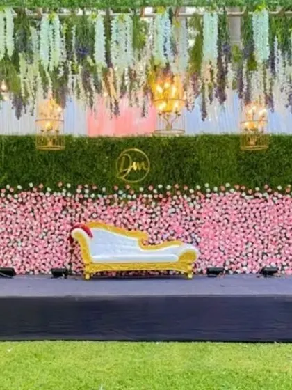 I designed this large-scale outdoor reception stage with a full-length flower wall of pink roses against a green hedge. The setup includes hanging floral installations and elegant chandeliers, creating a luxurious and romantic atmosphere.