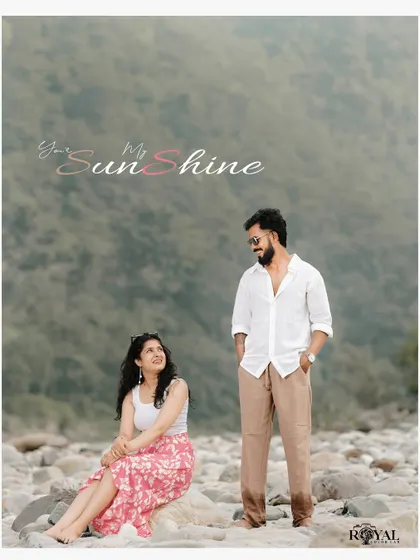 A sweet portrait of a couple on the rocky riverbank, with the man standing and the woman sitting, looking up at him lovingly.