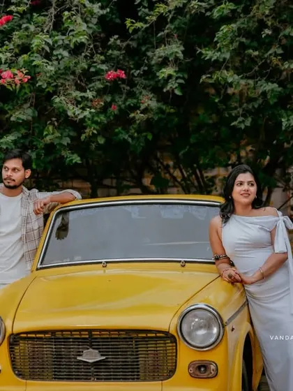 A cool, stylish pose with a couple leaning against a vintage yellow car, surrounded by greenery.