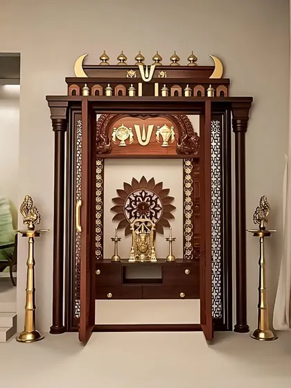 A grand and traditional pooja mandir crafted from dark wood with intricate carvings and brass details. The ornate doors open to reveal a sacred space, complete with traditional lamps.