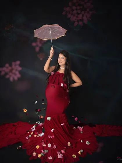 A whimsical and sweet portrait. The mom-to-be holds a delicate umbrella as flower petals rain down around her, adding a touch of magic to her red gown.