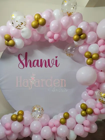 A simple and sweet circular backdrop with a custom name and a partial balloon garland in pink and white.
