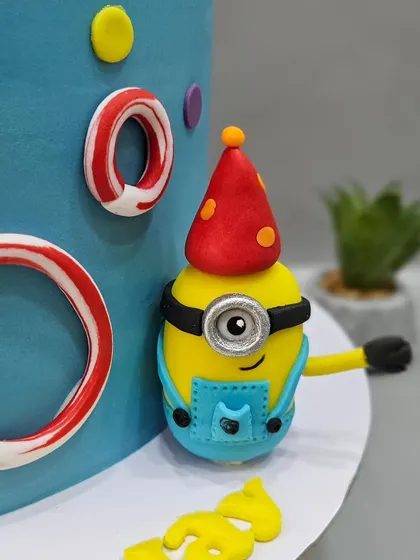 A close-up of the details on the Minion cake, including candy-striped letters and colorful dots.