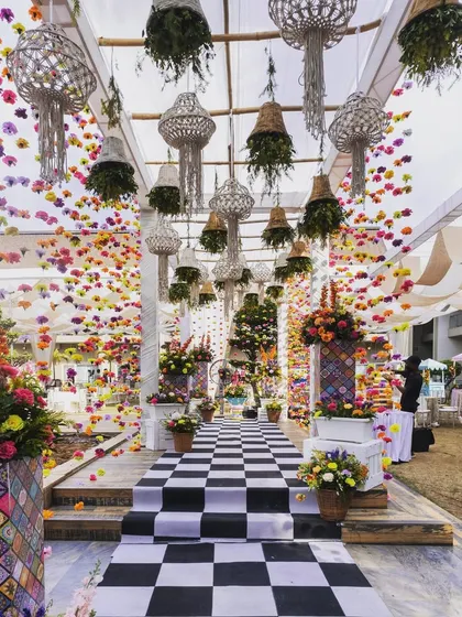 The grand entrance walkway for the carnival event, with a checkered floor and a ceiling adorned with hanging macrame planters and colorful flower strings.