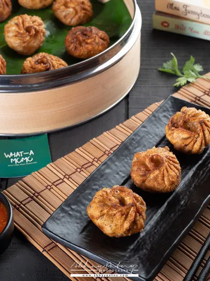 These fried momos are presented on a dark slate platter, which makes their golden, crispy texture the main focus. The bamboo mat and dipping sauce complete the Asian-inspired theme.