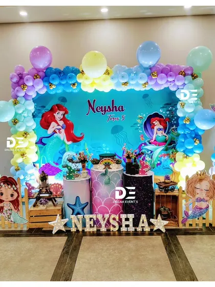 A 'Little Mermaid' theme for Neysha's 5th birthday. The stage is decorated with Ariel cutouts, an ocean-blue backdrop, and a colorful balloon arch, bringing the classic Disney movie to life.