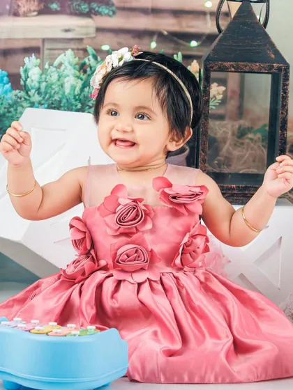 A happy baby girl in a pink dress, playing with a toy piano in a whimsical garden setting.