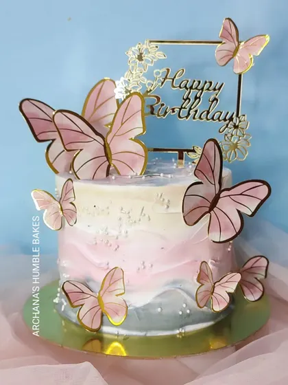 A pretty cake with a pink and grey watercolor effect, adorned with pink butterflies.