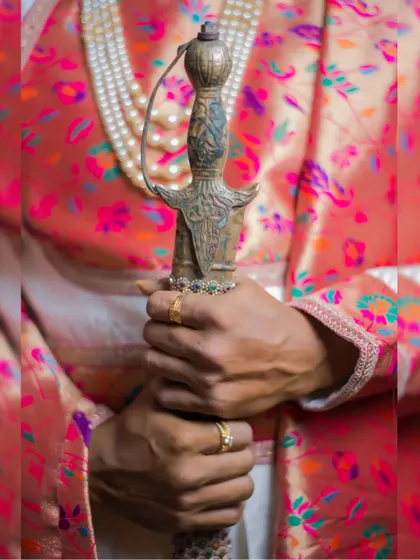 A close-up of the groom holding the hilt of his ceremonial sword, a detail that adds to the regal character of his wedding look.