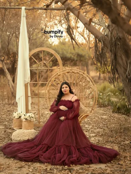 A solo portrait of the mom-to-be seated on the wicker peacock chair. The earthy tones of the background and her dress create a warm and inviting atmosphere.