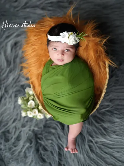 A beautiful portrait of a newborn girl, swaddled in olive green and wearing a delicate floral headband. Her direct gaze makes for a captivating and precious memory.